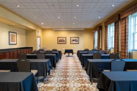 A classroom with rows of tables covered in black cloths. A table is in the center, a projector is above.