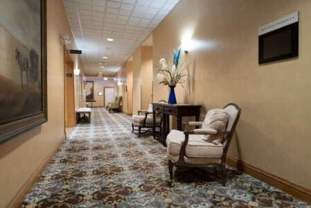 Hallway with beige walls, floral carpet, two chairs, and a dark table.