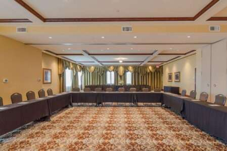 A conference room with a U-shaped table, beige walls, patterned carpet, and decorative curtains.