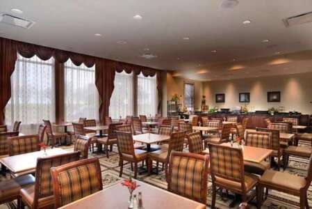 Restaurant dining room with square tables, plaid chairs, and large windows with brown curtains.