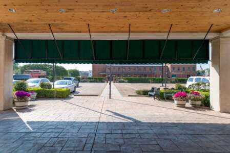 View from a covered entrance with green awning; cars parked outside, flowering plants in pots.