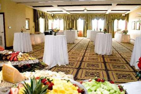 Buffet setup in a banquet hall with white-covered cocktail tables and patterned carpet. Food displays in the foreground.
